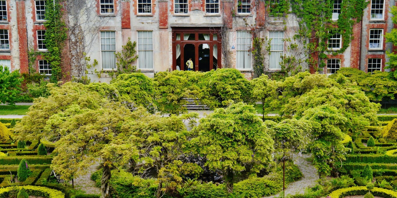 A large stone house seen from the garden side, with lawns and planting running up to the front of it.