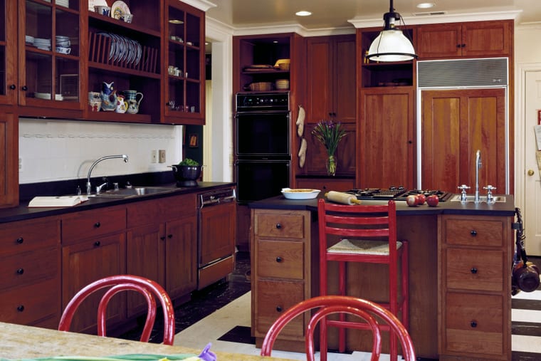 A fitted kitchen in dark cherry timber with a glazed dresser, stone worktops and a central island.