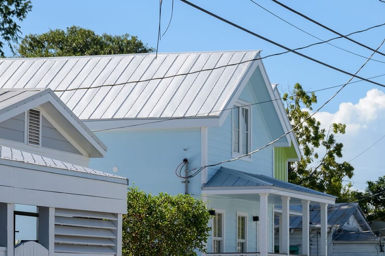 A pale timber house with a standing-seam metal roof and a columned veranda under a clear sky.