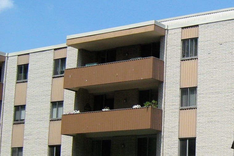 Stacked balconies on the face of a pale brick apartment building, seen against a clear sky.