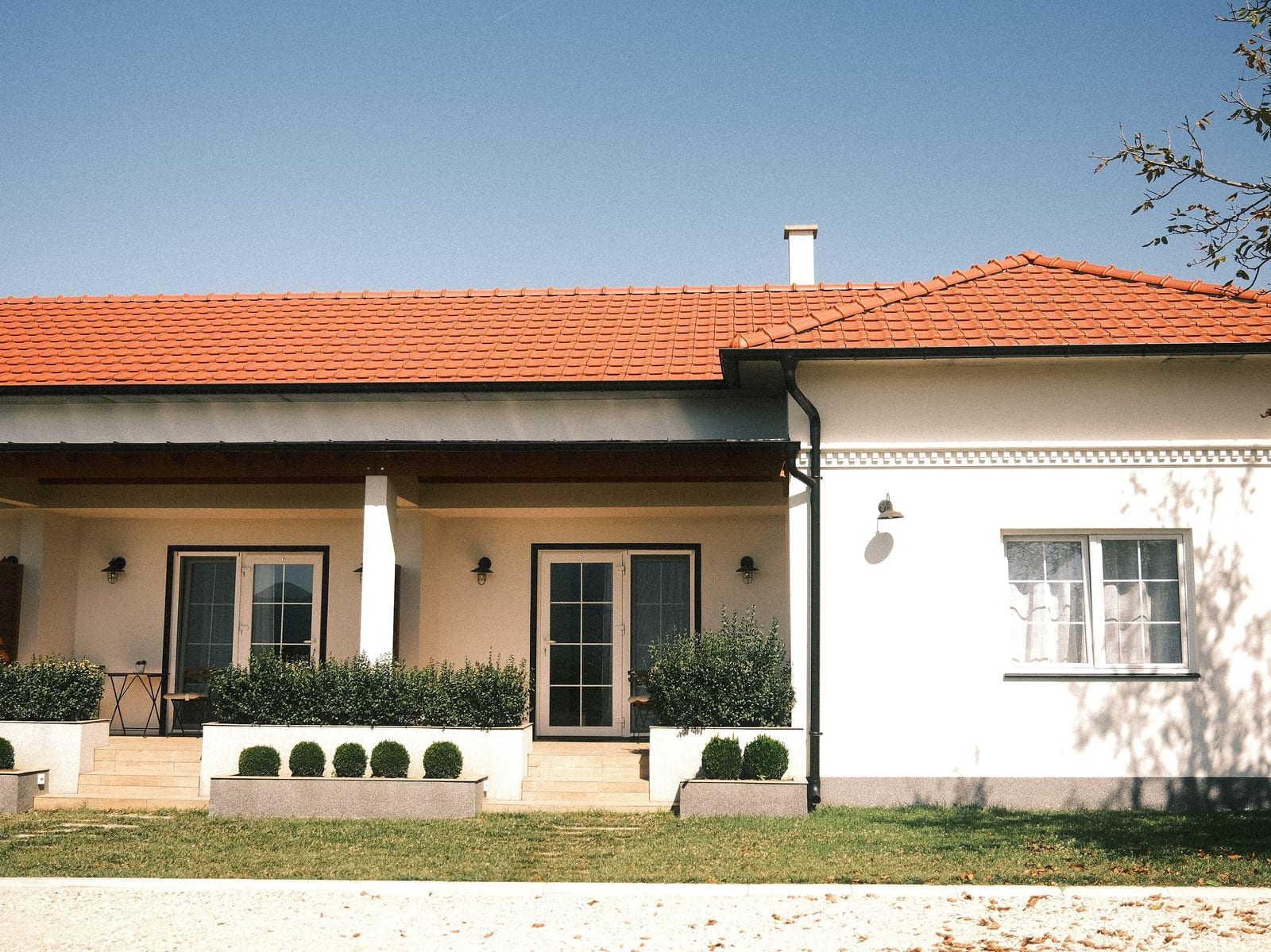 A modern house with a red roof standing behind a landscaped garden under a clear sky.