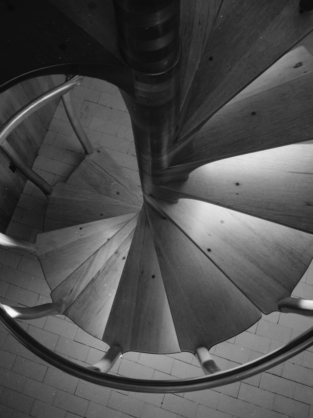 A timber spiral staircase photographed from above, its curved handrail sweeping past the treads.