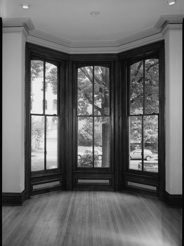 A bay window of three tall sashes in dark joinery, above a bare boarded floor.