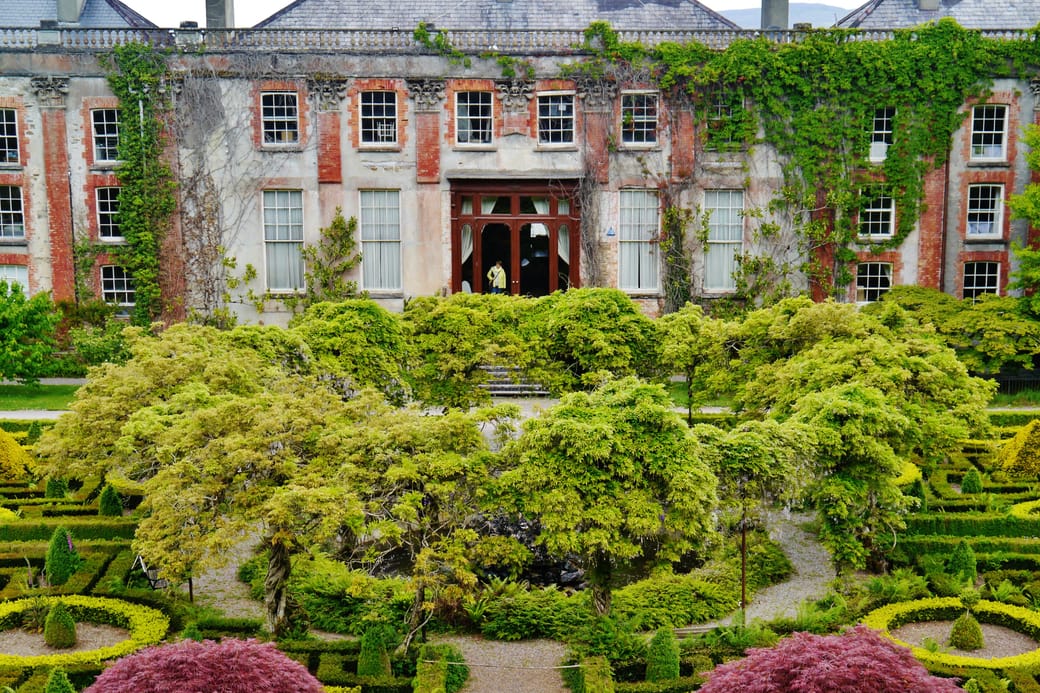 A large period country house seen across formal lawns and clipped hedges.