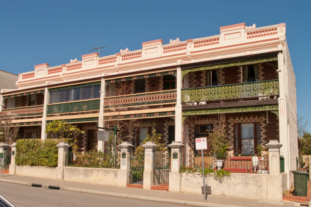 A two-storey terrace with iron lace verandas standing behind a low rendered front wall.