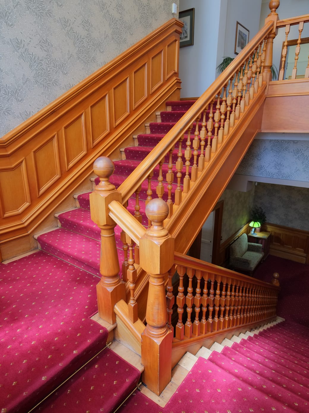 A wooden staircase rising through the panelled hall of a period house.