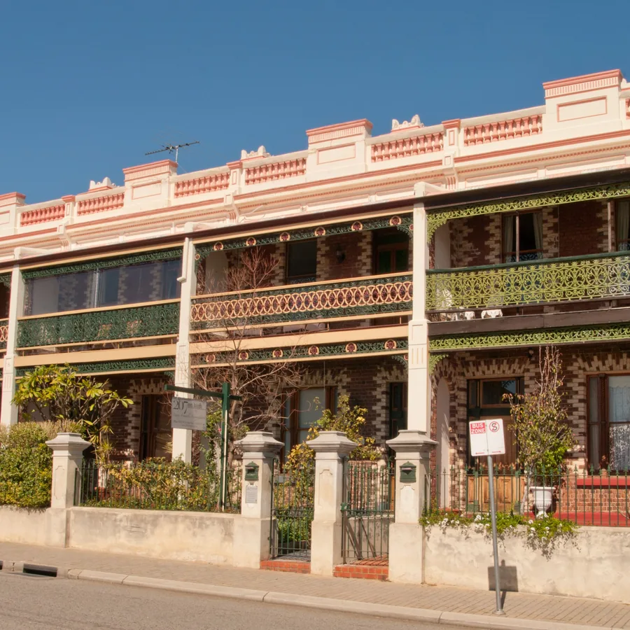 Two-storey terraced houses with iron verandahs behind a front fence