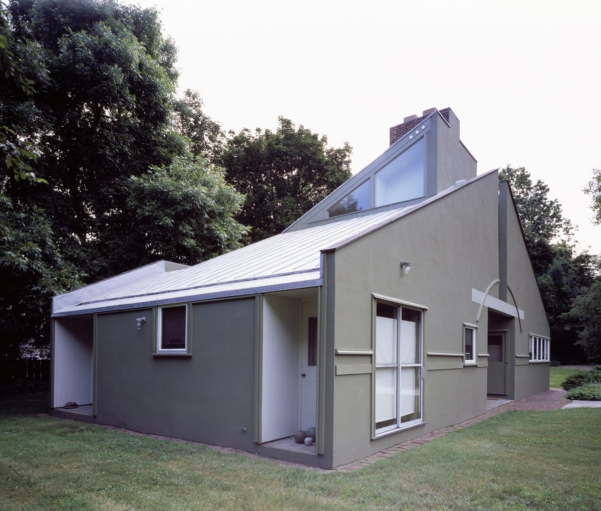 An eco-modern house with a sculpted pale grey facade set among tall green trees
