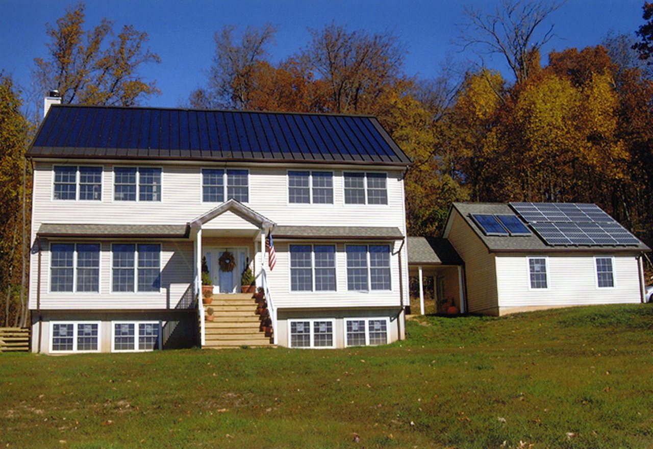 The Meadowlark — a white clapboard cape with a dark solar roof and a solar outbuilding, Cedar Hollow, OR
