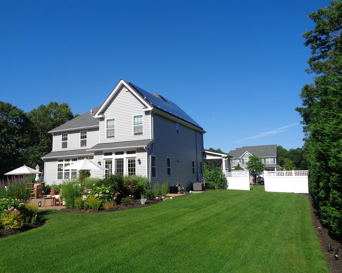 A white two-storey home with roof solar seen across its back lawn