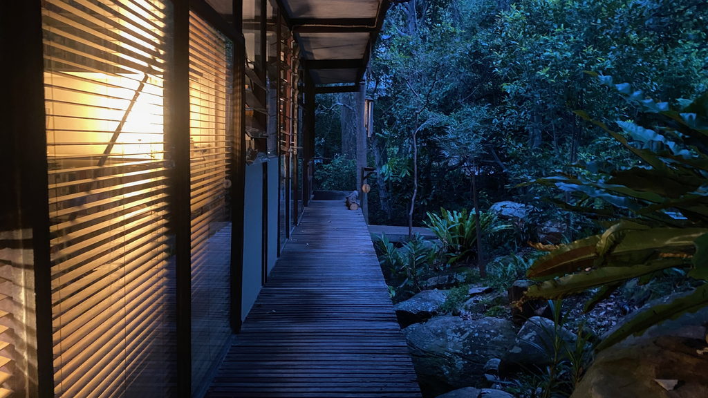 Lit glass-walled pavilion residence seen from the garden at dusk