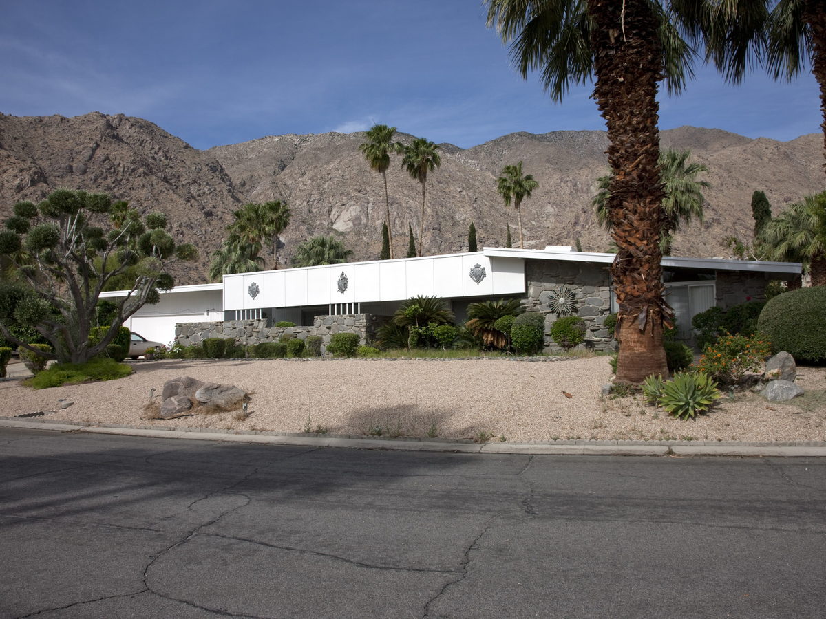 Long low desert-modern house behind a boulder garden