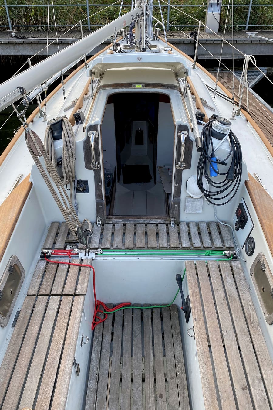 Looking forward through the cockpit of a small sailing yacht: teak slatted seats, winches and the open companionway.