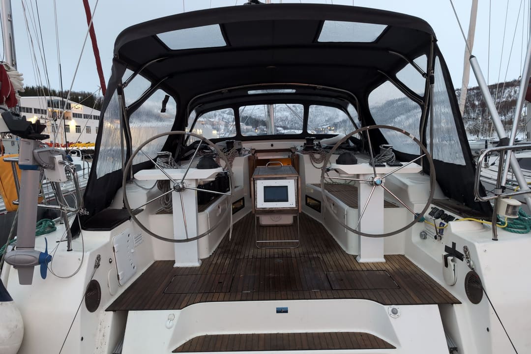 The wheel cockpit of a sailing yacht under a dark bimini, with a teak sole, moored in a marina.