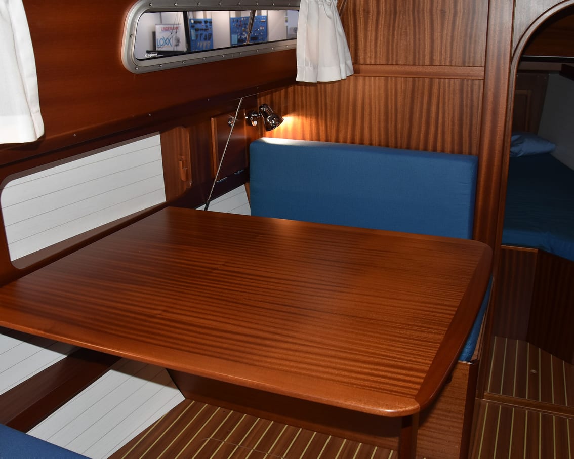 A varnished saloon table below deck, with a blue upholstered berth running along the side of the cabin.