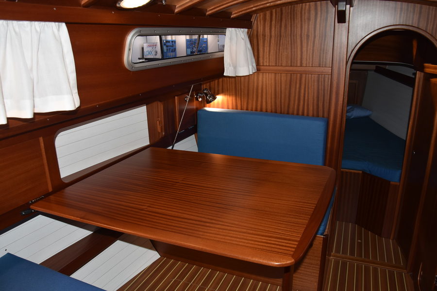 A varnished timber saloon with a folding table and blue upholstered berths.