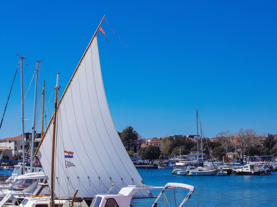 A traditional rig with its sail hoisted alongside a quiet marina pontoon.
