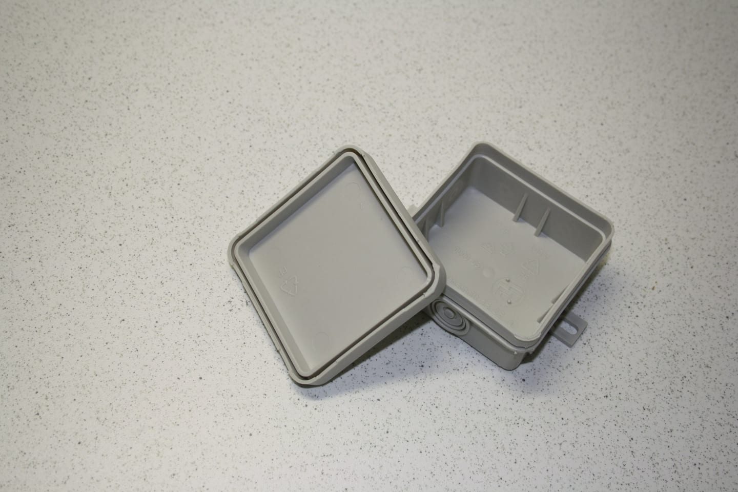 A grey weatherproof junction box open on a bench, its lid resting beside the gasketed base.