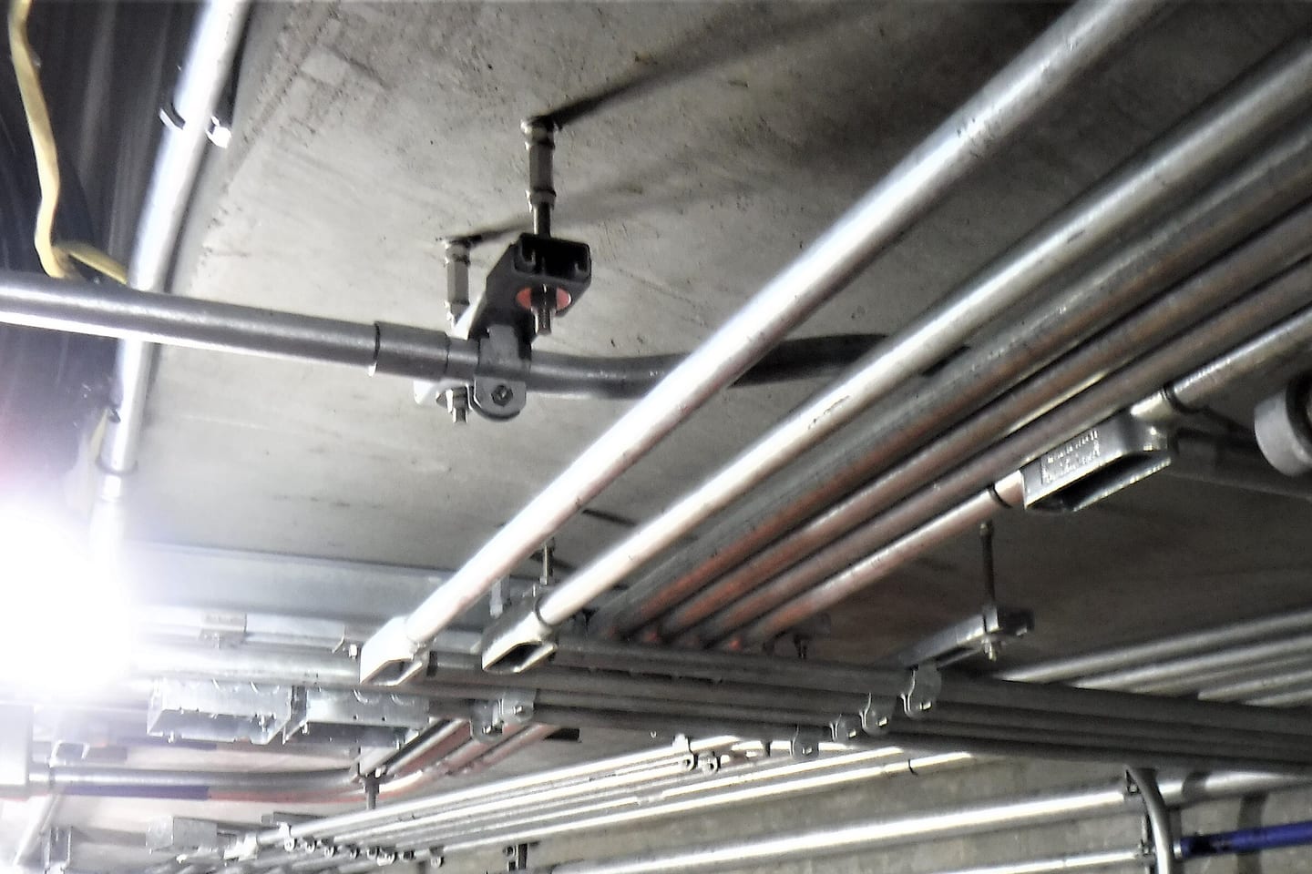 Galvanised conduit runs fixed to a concrete soffit, with a cable hanger clamped to one of them.