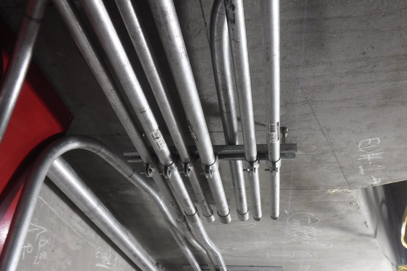 Power-feed conduits bent down from a concrete soffit and clamped in a row along a support channel