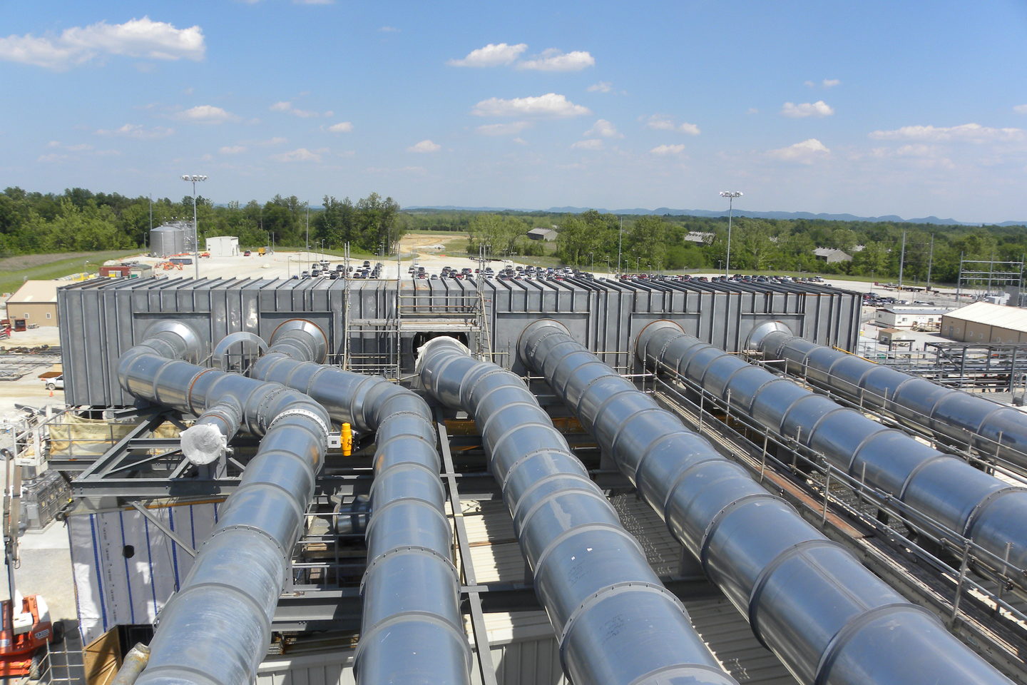 A plant room walkway between large pale ducting and insulated pipe runs, lit from overhead