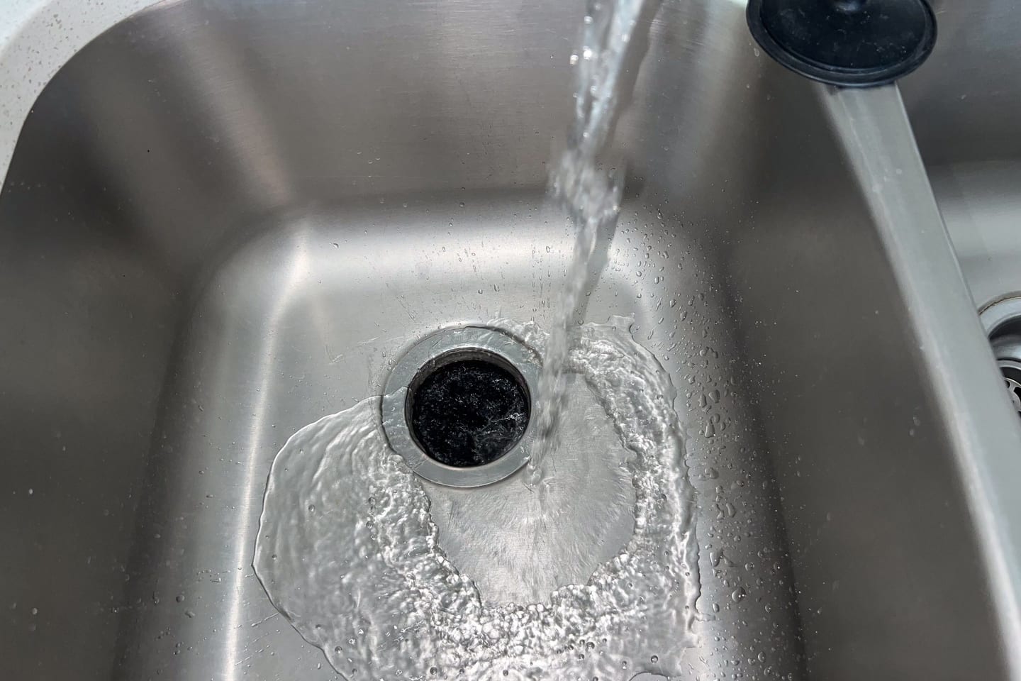 A stainless steel sink basin with a mixer tap above it and the waste disposal unit fitted beneath