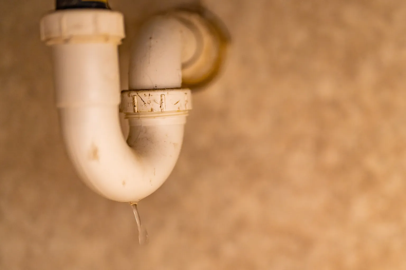 Failed PVC drain trap beneath a sink with the joint separated for replacement