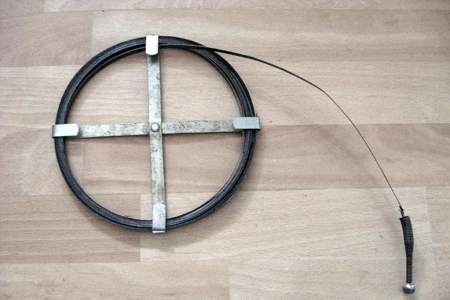 A coiled drain auger with its cable head extended on a floor