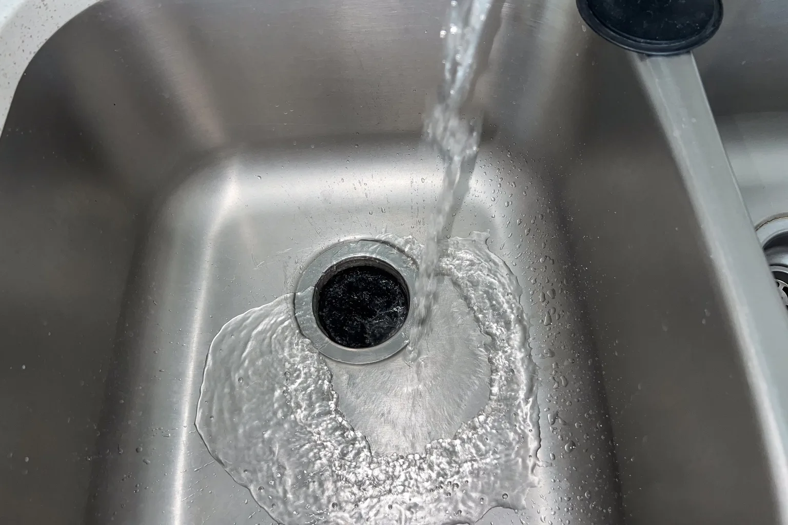 Clear water running into a stainless kitchen sink during a drain flow check