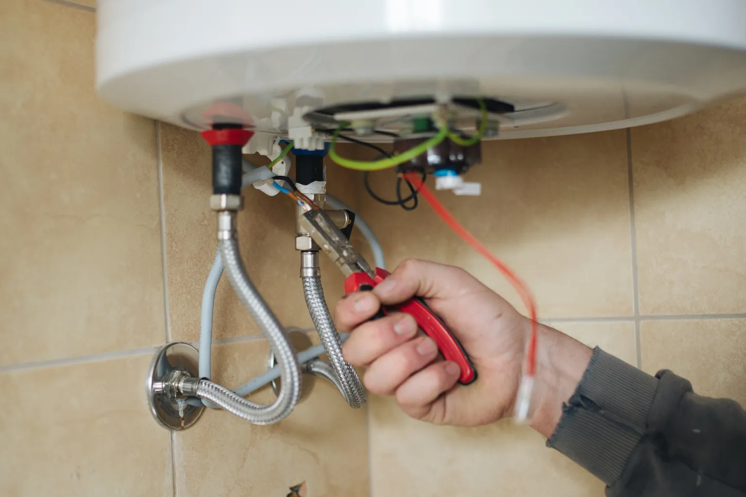 Water-heater connections checked with pliers at a wall-mounted unit