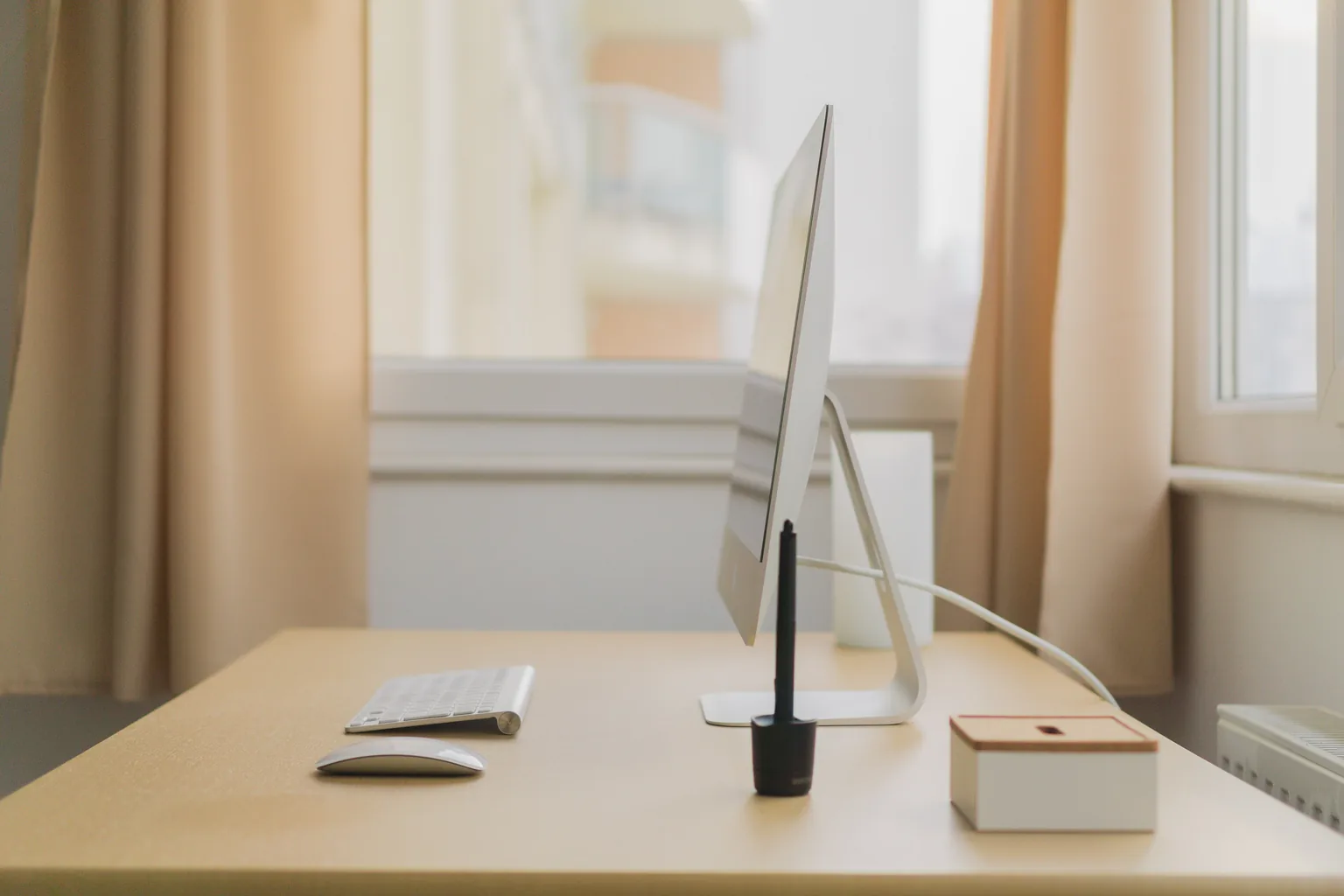 Tidy desk with a monitor, keyboard and note box by a window