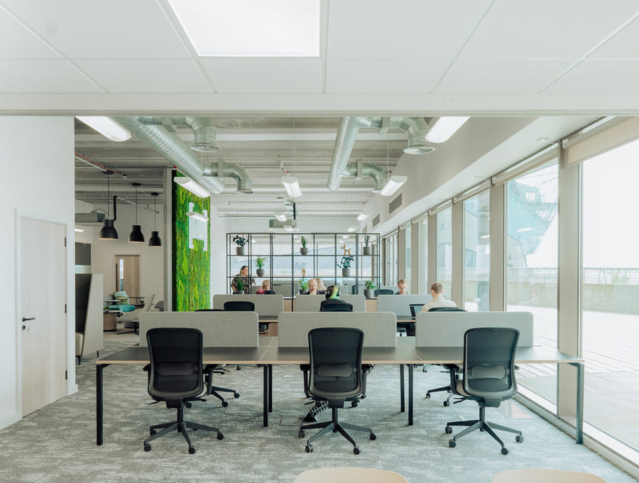 An open-plan office floor of desks and monitors behind a glazed partition