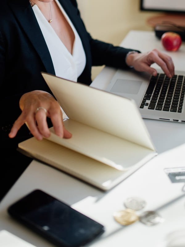 A hand opening a cream document folder beside an open laptop on a white desk