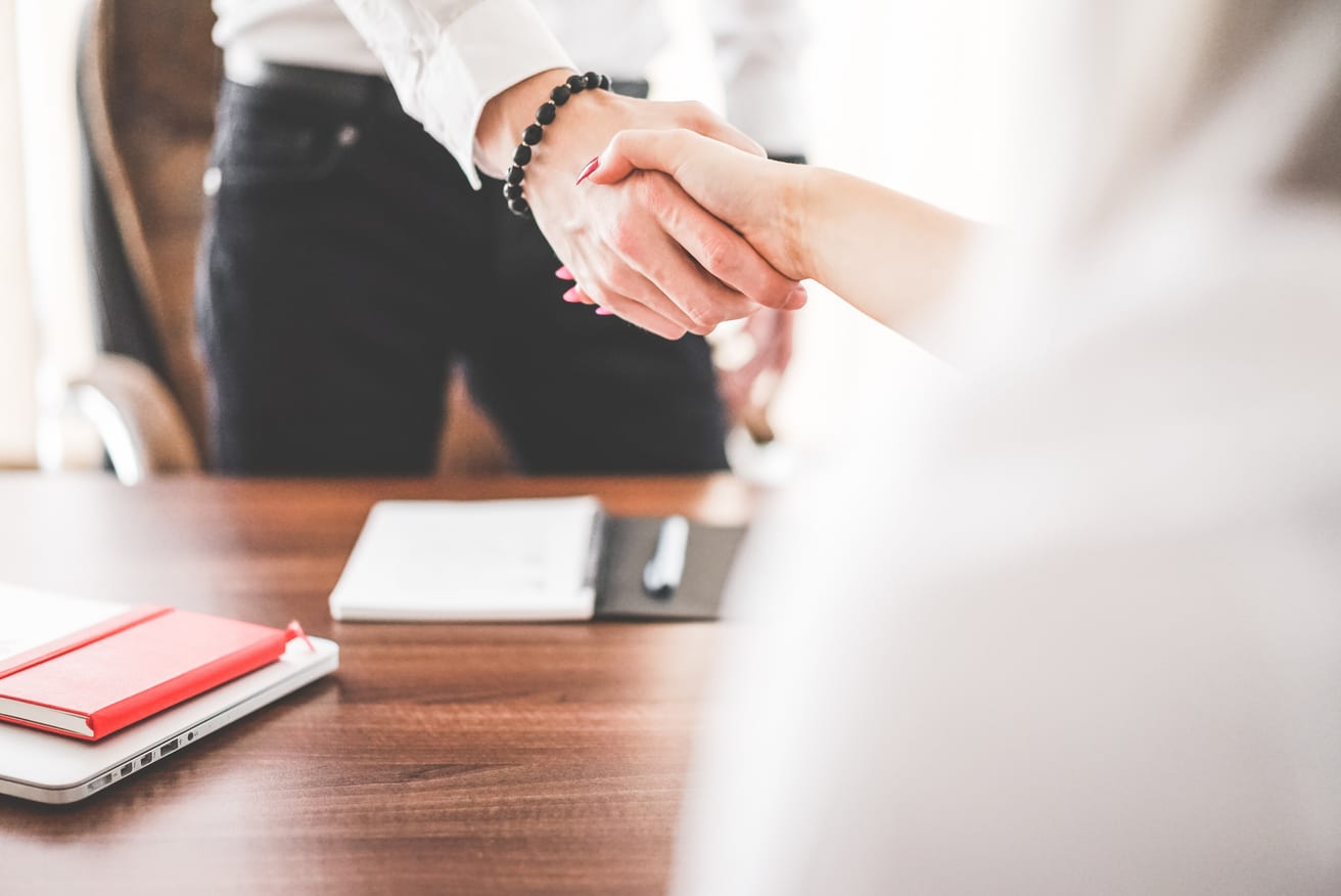 Two people shaking hands across an office desk, shown without their faces.