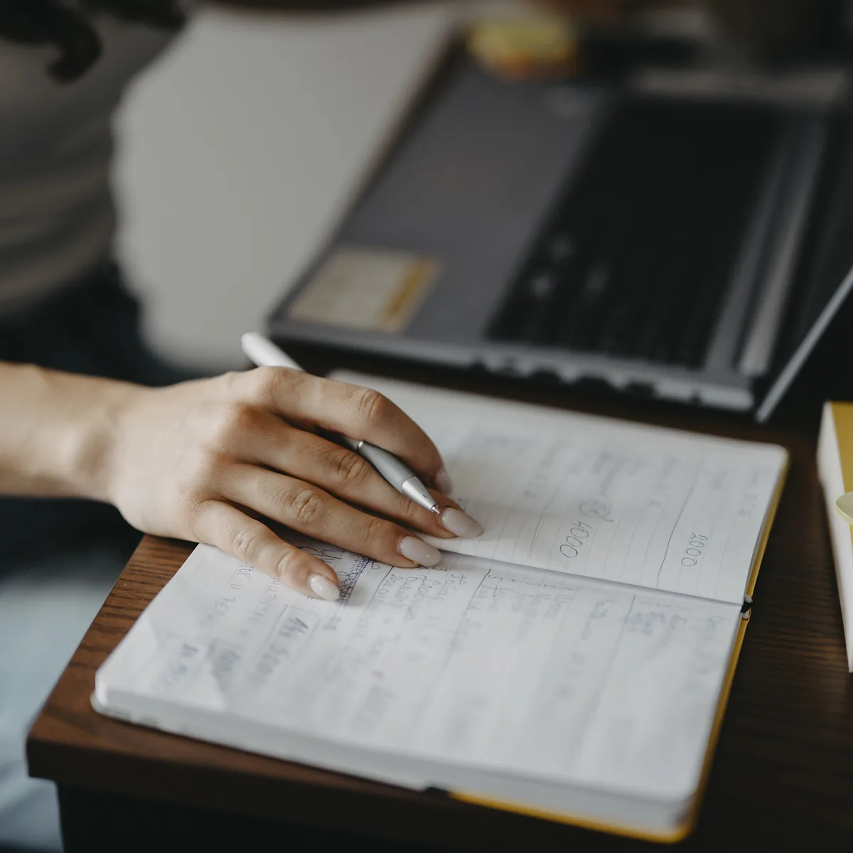 Figures written into a ruled notebook beside a laptop
