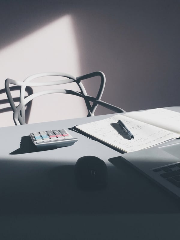 A desk with a laptop, a calculator and an open notebook with a pen