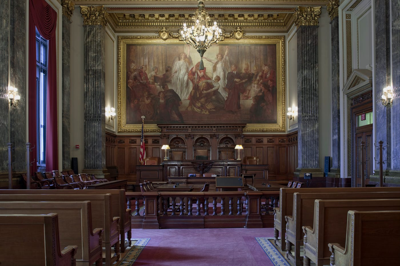 A panelled federal courtroom with a mural above the bench, a carved rail and wooden benches.