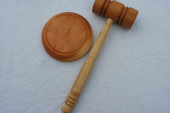 A wooden gavel lying beside its round sounding block on a pale grey cloth.