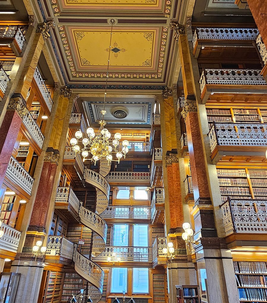 Spiral iron staircases and book balconies rising toward a painted library ceiling.