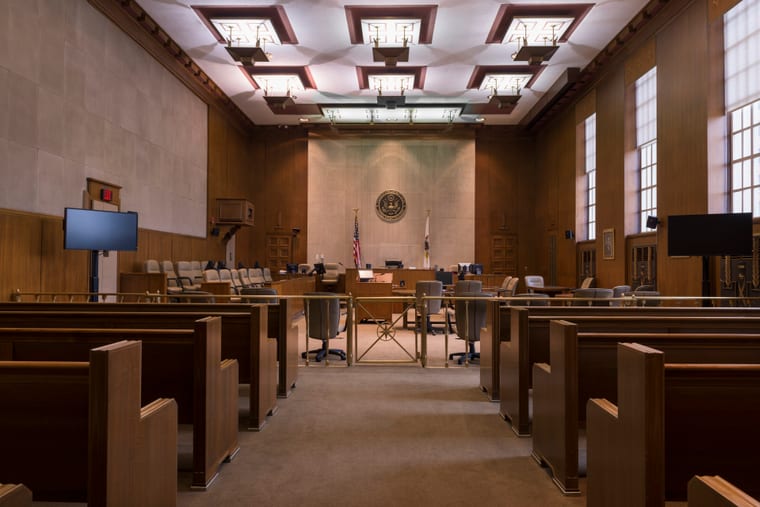 An empty courtroom with fixed benches, a raised bench and panelled walls.