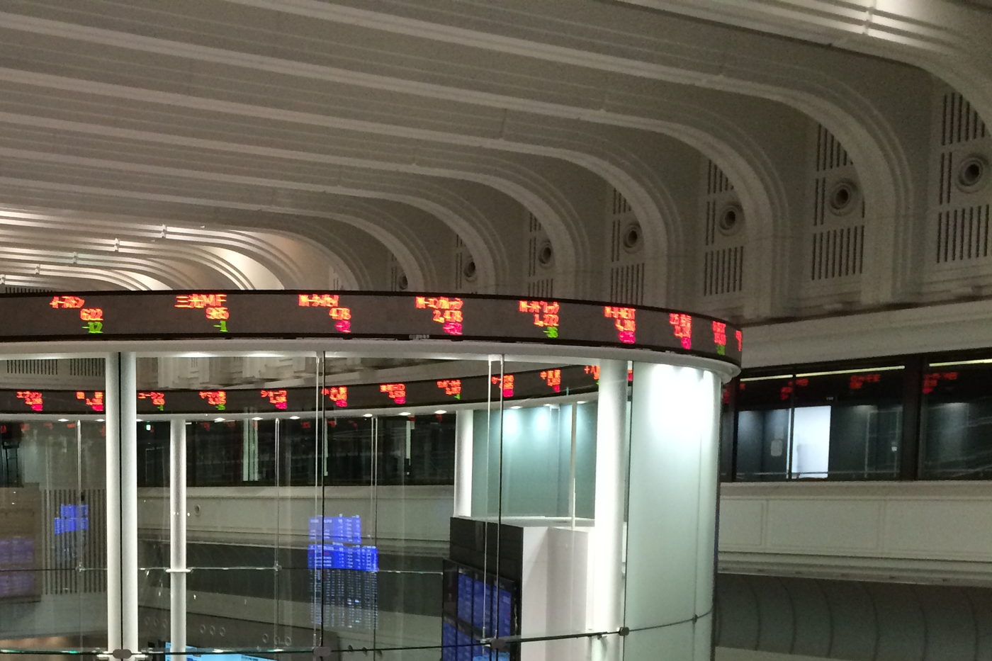The trading floor of a stock exchange, a circular ticker band of stock codes running around a glazed drum under a vaulted ceiling.