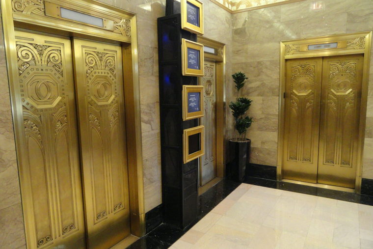 Polished brass lift doors set into a marble lobby wall, lit from above.