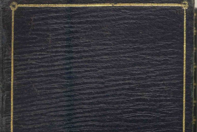 The corner of a dark navy leather book cover with a thin gold line tooled around its edge.