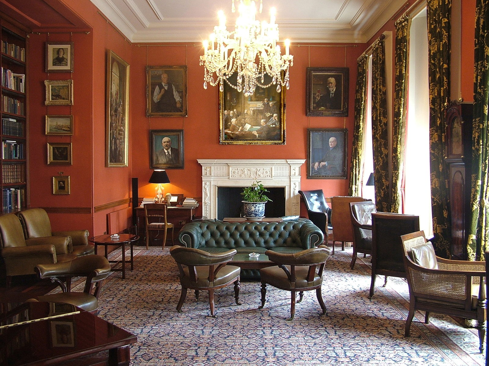 A private drawing room with dark red walls, a lit chandelier and upholstered chairs drawn up around a low table.
