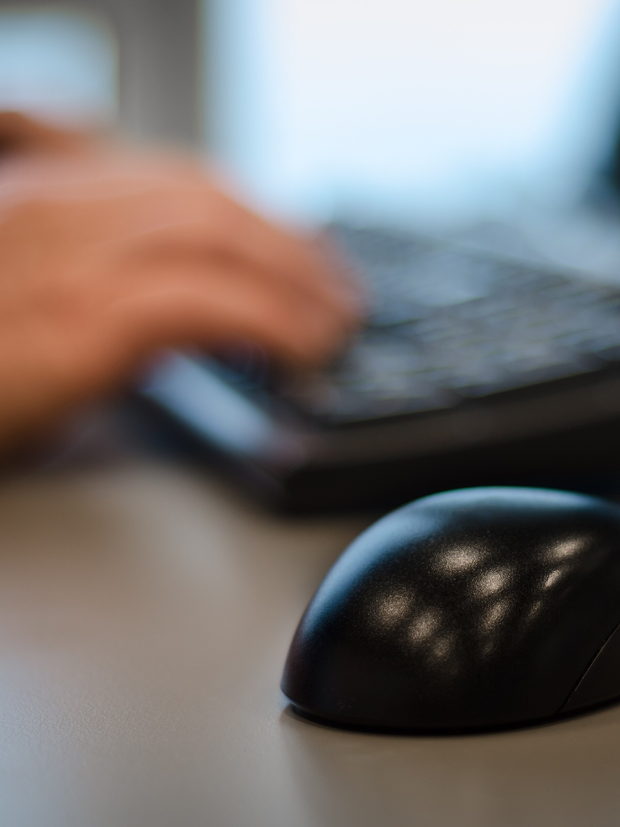 A pair of hands at a keyboard on a desk, photographed close and in shallow focus.