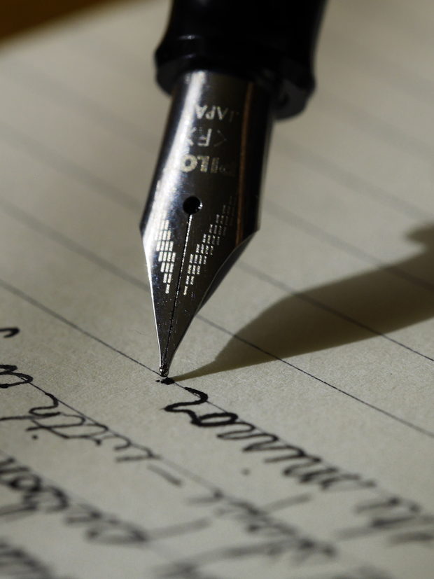 The nib of a fountain pen resting on a sheet of handwritten ruled paper.