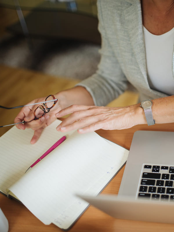 An adviser turning the pages of a notebook beside a laptop, reading glasses in hand