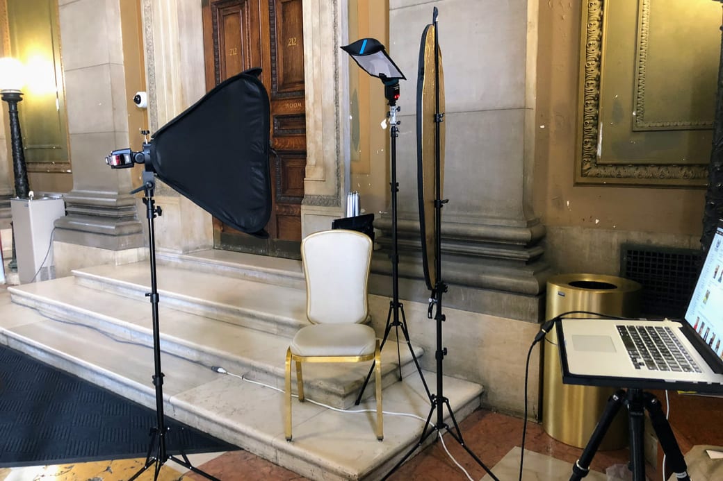 A softbox, a white chair and a laptop set up as a temporary portrait studio in a large panelled room.