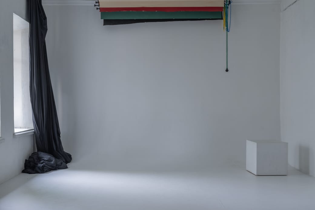 A working studio with a rail of rolled paper backdrops along one wall, a black curtain drawn beside them and a white cyclorama sweep at the far end.