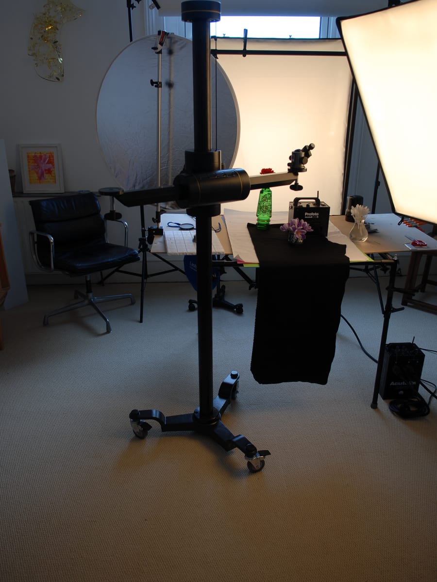 A small photography studio with a lighting stand, a folded reflector and a stool standing ready on a bare floor.